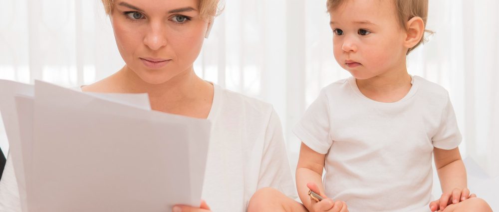 A mother reading paper and a baby watching